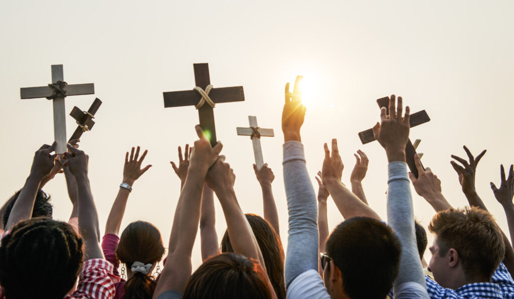 Christians with their hands in the air outside while holding wooden crosses