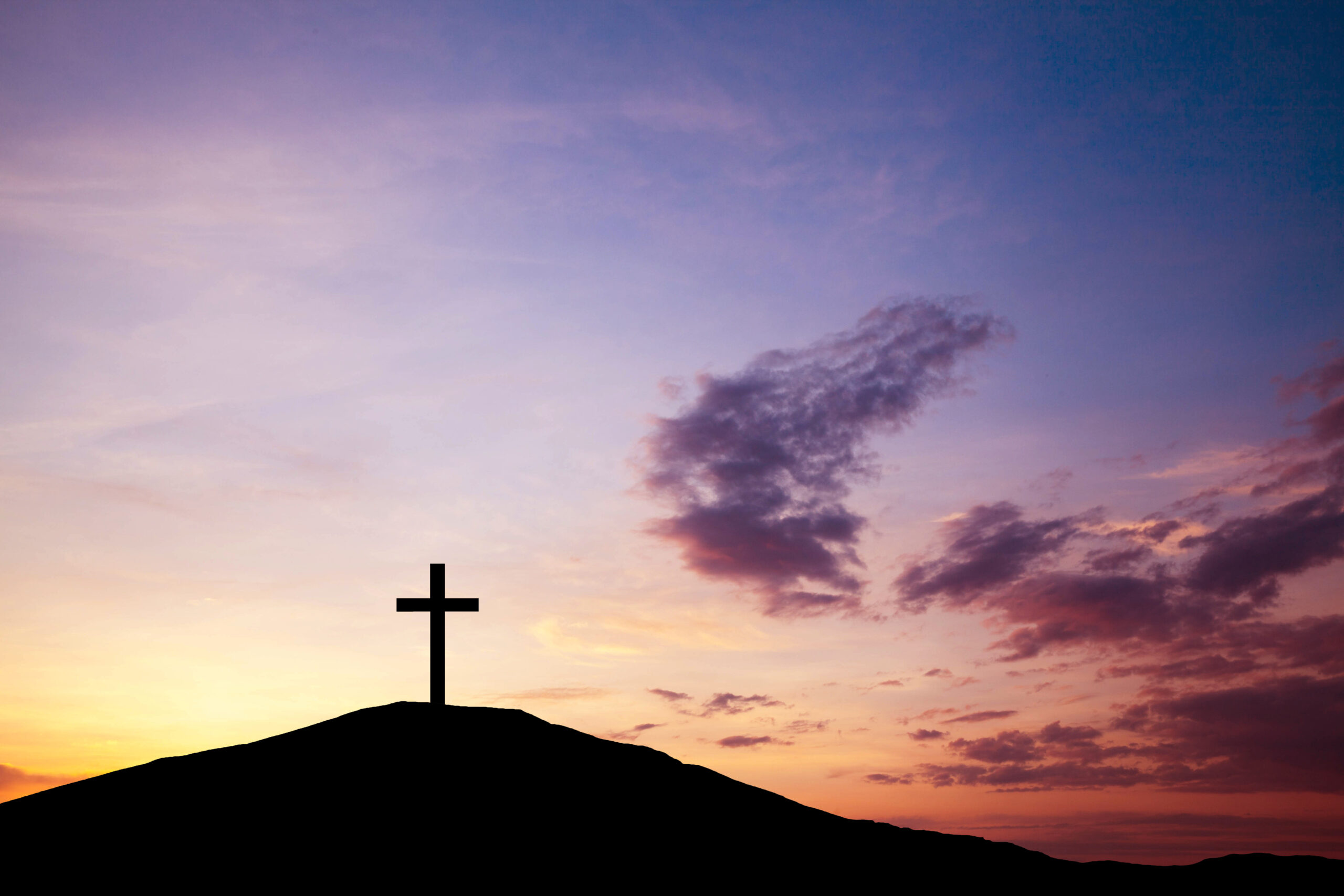 A single cross standing at the top of a hill while the sun sets