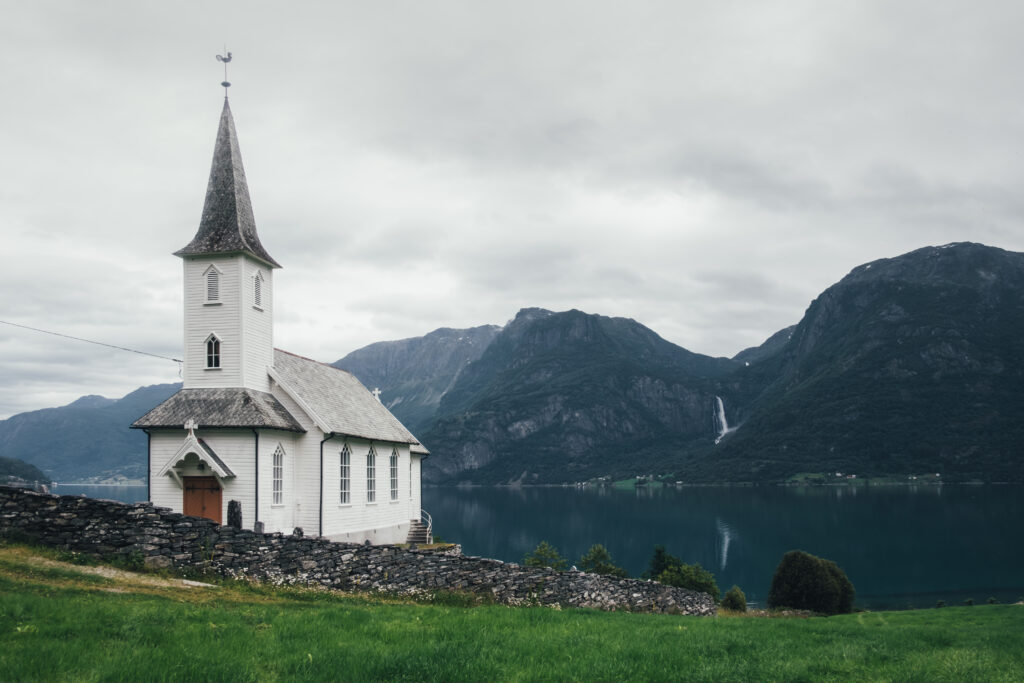 A beautiful landscape on a cloudy day with an old white church and green mountains in the background